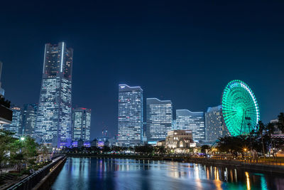 Illuminated buildings by river against sky in city at night