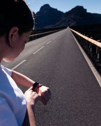 Young woman checking time while standing on road