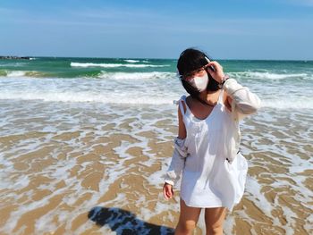 Rear view of woman standing at beach against sky