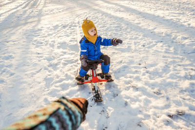 Cropped hand of father pulling boy sitting on sled over snowy land