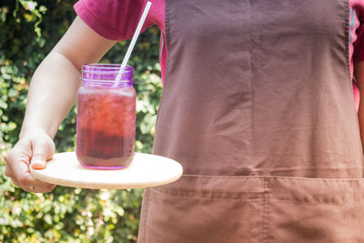 Midsection of woman holding drink in jar on cutting board