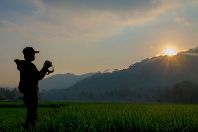 Man standing on field against sky during sunset