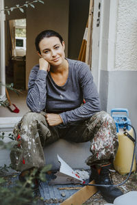 Full length portrait of smiling female carpenter sitting at doorway of house