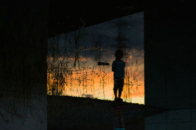 Silhouette man standing by wall against sky at night