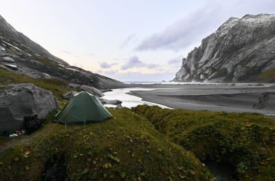 Green tent on hill at bunes beach during sunset with mountains and the ocean  lofoten norway