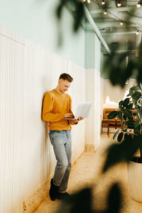 Side view of young man using mobile phone against wall