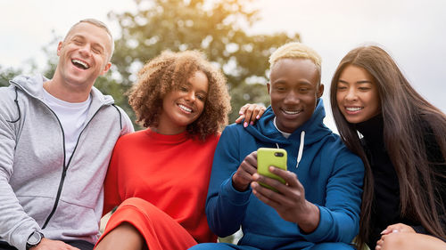 Smiling friends looking at phone sitting on bench at park