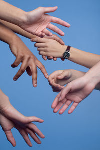 Cropped hands of people against clear blue sky