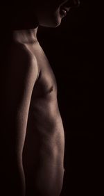 Midsection of shirtless woman against black background