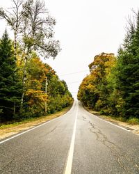 Empty road along trees and against clear sky