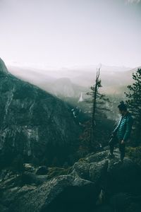 Side view of man with camera standing on cliff during foggy weather
