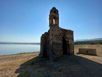 Old ruin building by sea against clear blue sky