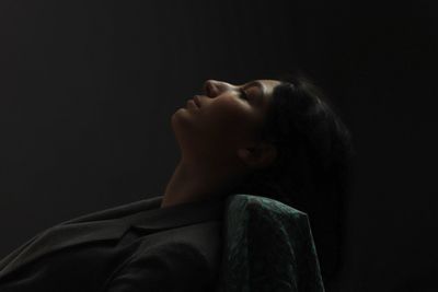 Side view of thoughtful woman sitting against black background