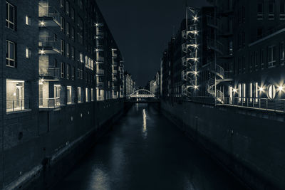 Illuminated bridge over canal amidst buildings in city at night