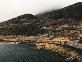 People walking on mountain by lake against sky