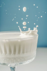 Milk pours into a beautiful crystal glass on a blue background and splashes around.