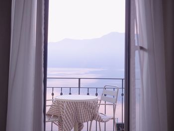 Empty chairs with table arranged in balcony against sea seen through window