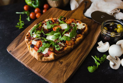 Close up of handmade pizza on wooden board with ingredients around it.