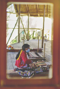 Rear view of woman sitting on window