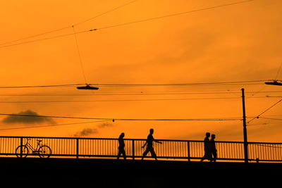 Silhouette people walking on bridge against orange sky during sunset