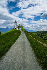 Road passing through field against cloudy sky