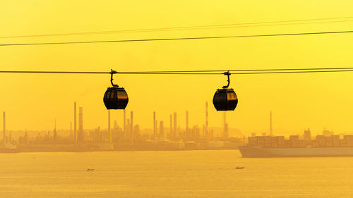 Cable cars over river against sky during sunset