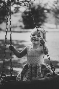 Portrait of smiling girl sitting on swing at playground