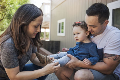 Father carrying baby while mother assisting in wearing shoes