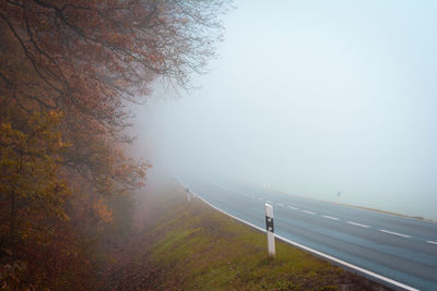 Road by trees against sky during autumn