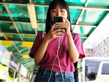 Low angle view of young woman using mobile phone while standing in city