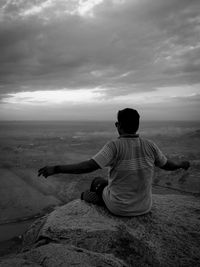 Rear view of man sitting on land against sky