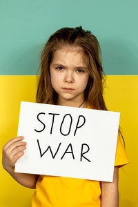 A girl is crying, holding a stop poster on the background of the ukrainian flag. 