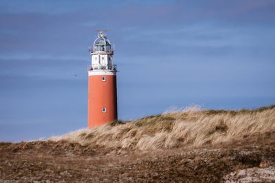 Lighthouse on field by building against sky