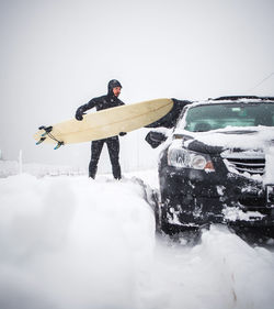 Surfer putting surfboard on top of car during winter snow storm