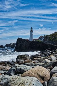 Lighthouse on rocks by sea against sky