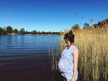 Rear view of woman standing by lake against sky