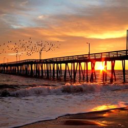 Silhouette bridge over sea against sky during sunset