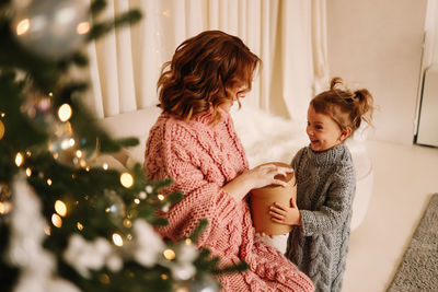 Happy mom and little daughter baby in sweaters hugging getting ready for  christmas holiday at home