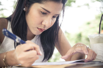 Close-up of young woman writing on paper at table