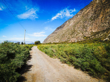 Road passing through field against cloudy sky