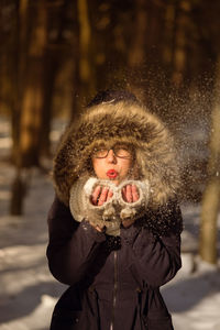 Portrait of young woman blowing snow on field