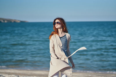 Young woman standing at beach against sky