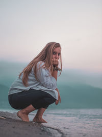 Portrait of beautiful young woman on beach against sky during sunset