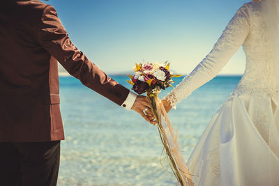 Low angle view of people standing by sea against sky