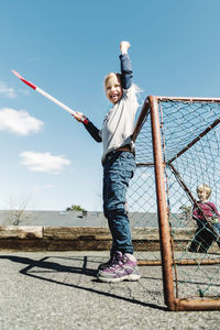 Low angle view of successful girl holding hockey stick against blue sky