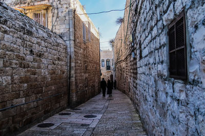 Rear view of people walking on footpath amidst buildings