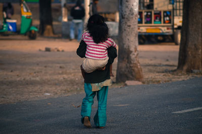 Rear view of mother piggybacking daughter on road