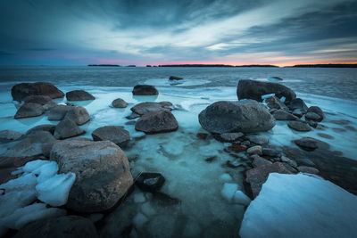 Rocks in sea against sky during sunset in finland.