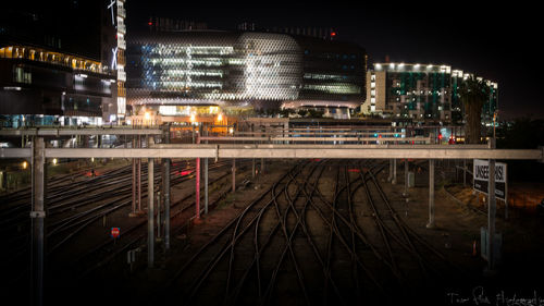 Railroad tracks by illuminated buildings in city at night