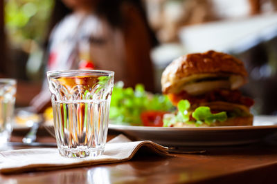 Drinking glass by burger in plate on table